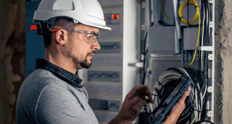 Um homem com capacete e óculos de segurança trabalhando em um painel elétrico