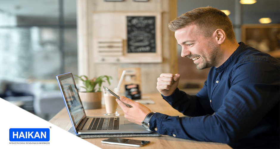 Homem comemorando em frente a um celular e um notebook